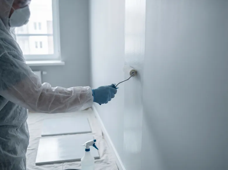 Technician in PPE applying a preventative treatment to a clean apartment wall